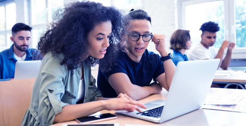 students in shared work space looking at a laptop