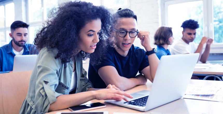 students in shared work space looking at a laptop